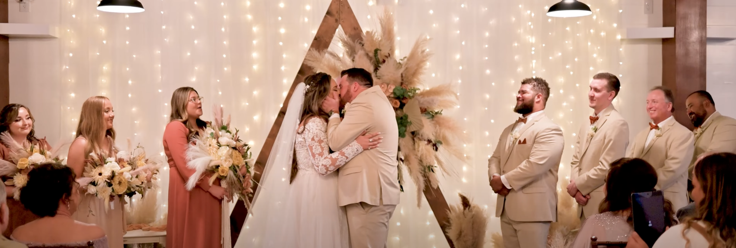 Wedding ceremony with string lights and white decor in the background.