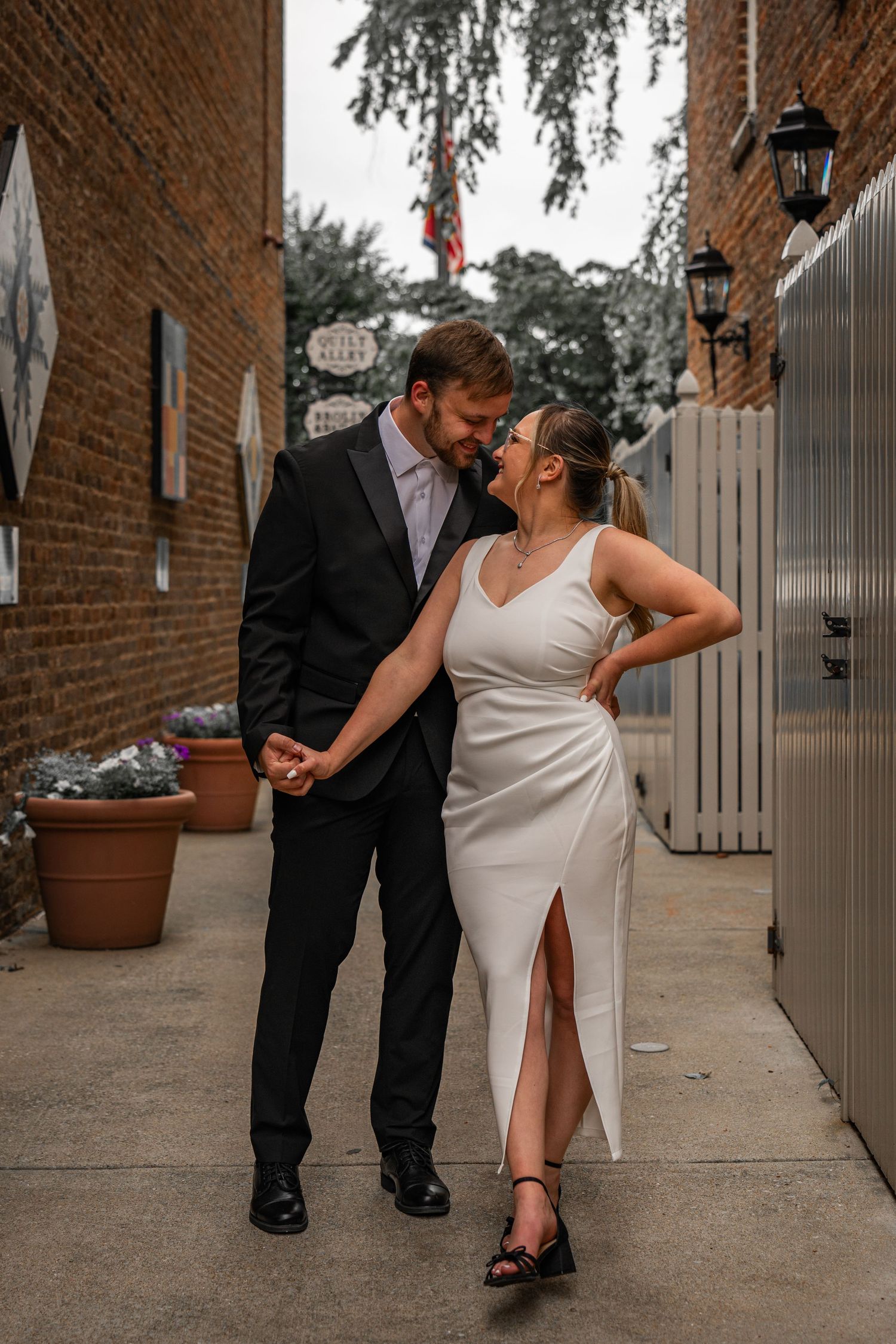 Romantic dance poses between couple in formal attire against brick building backdrop.