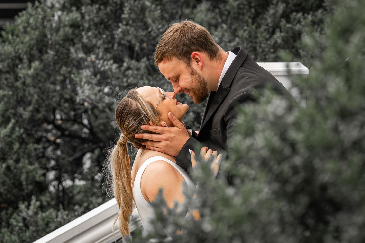 Romantic outdoor wedding portraits with couple embracing against greenery.
