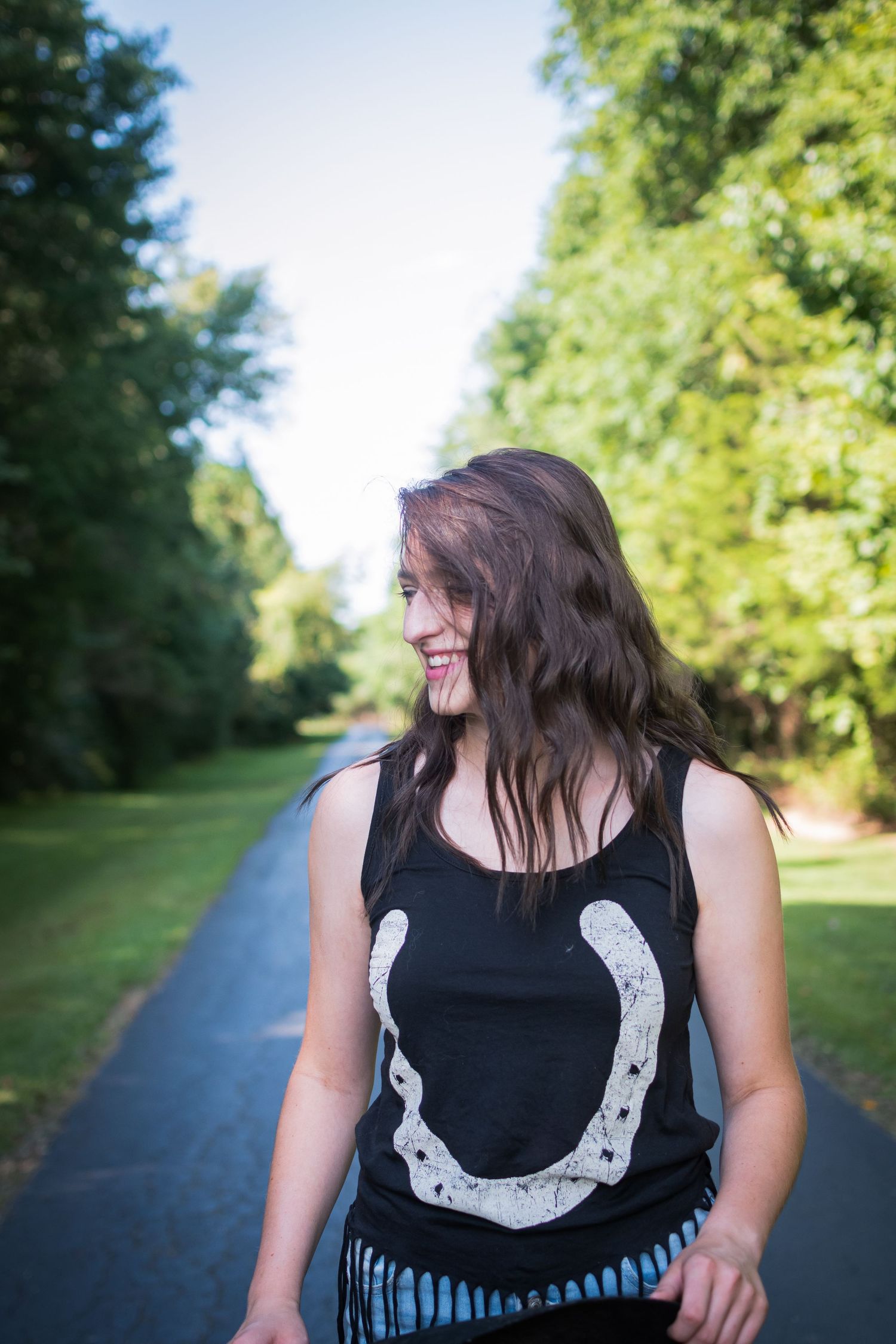 A path through green trees with a figure wearing a black tank top with white design.