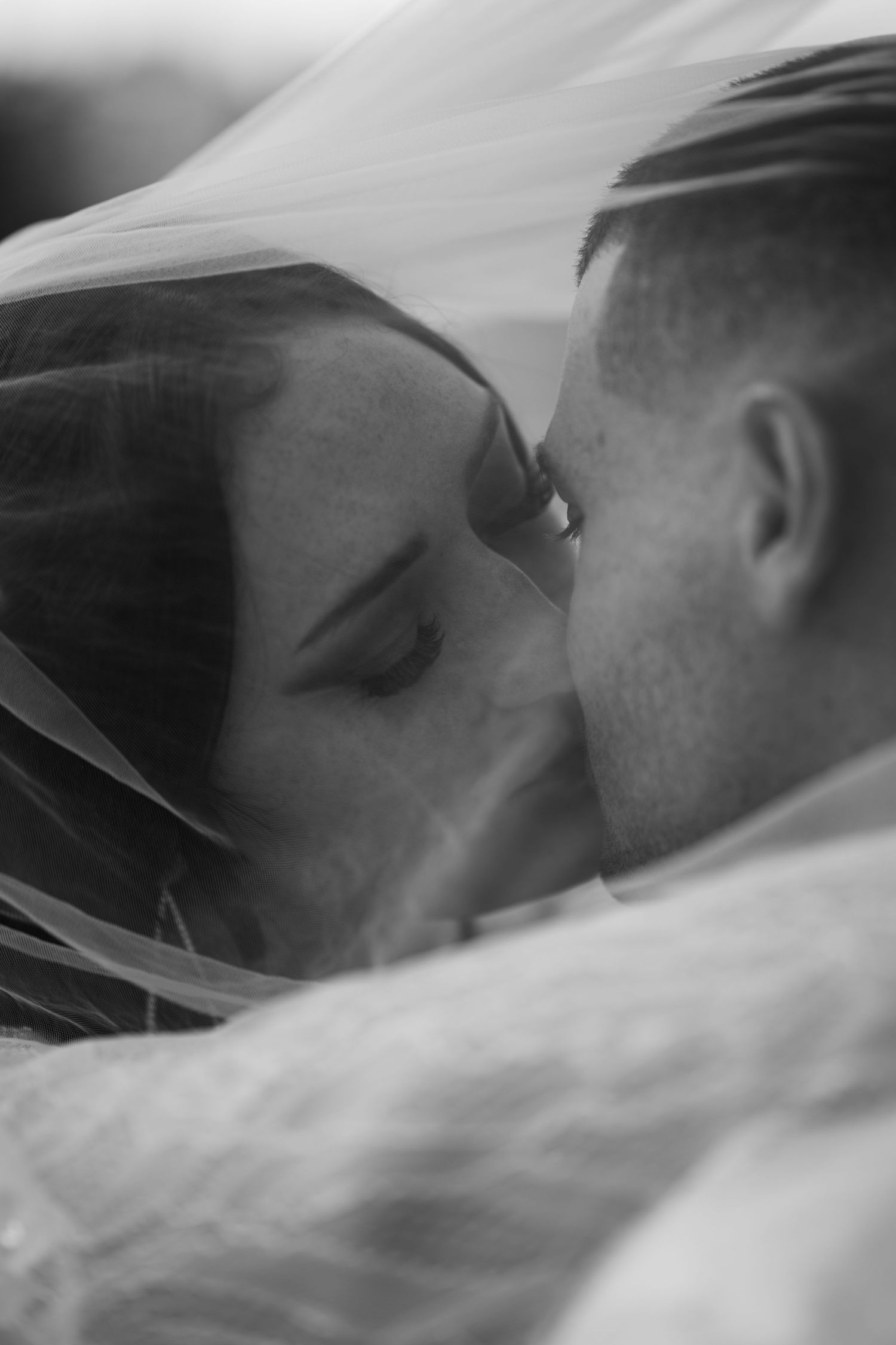 An intimate black and white wedding portrait with a delicate veil creating a dreamy effect.