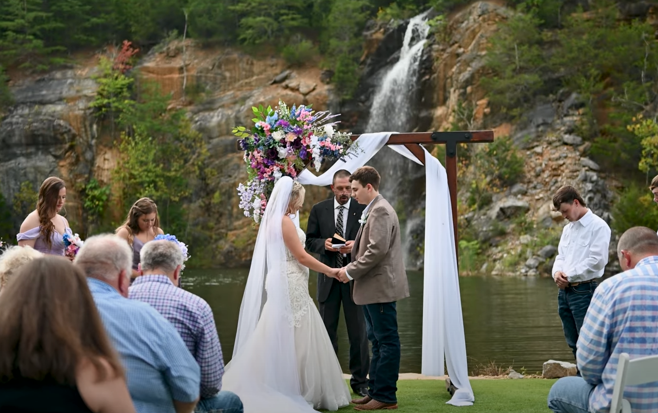 Wedding ceremony setup with white drapes and natural waterfall backdrop.