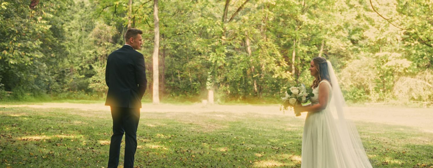 Wedding couple standing apart in sunlit garden setting.