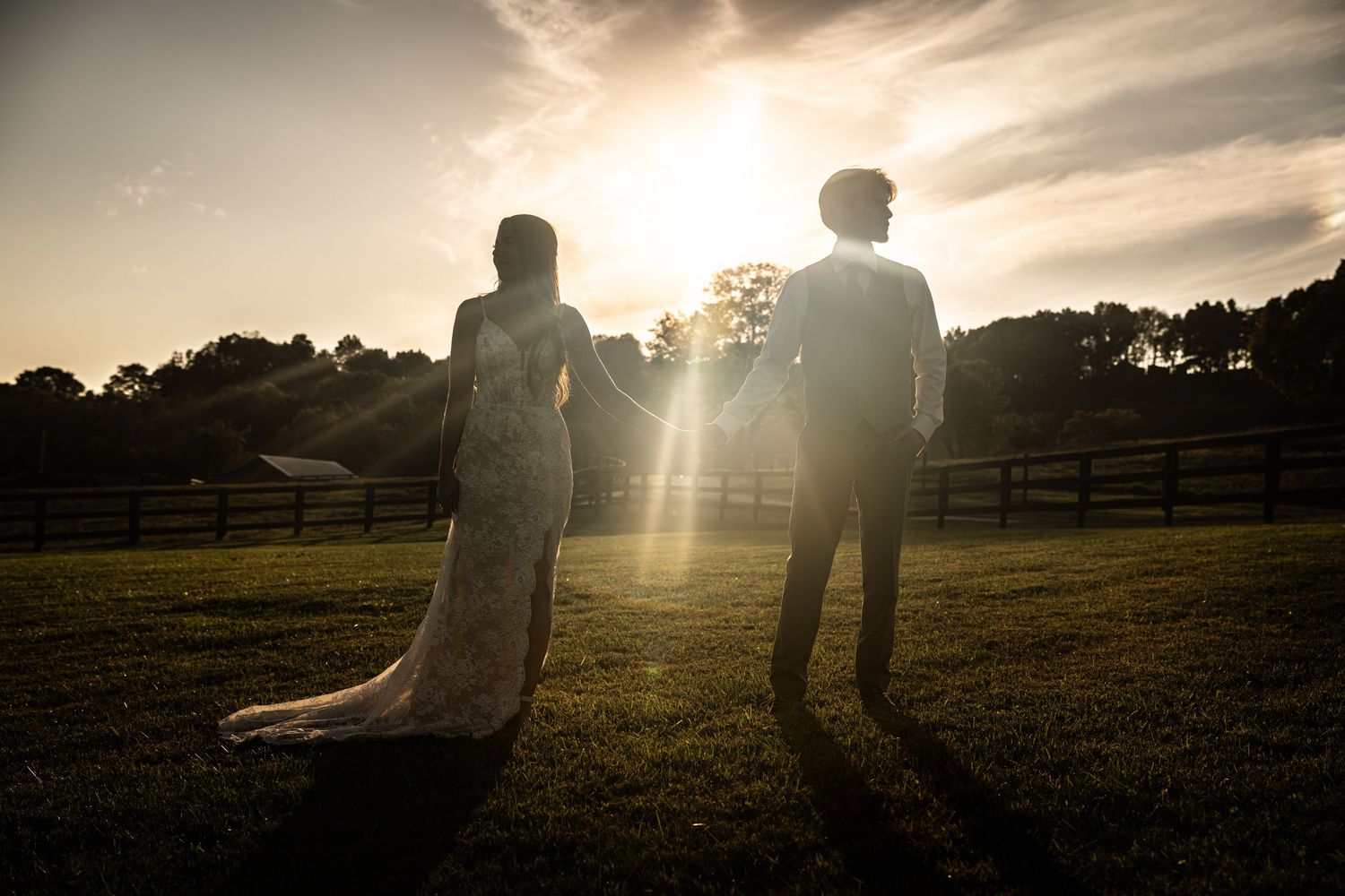 Silhouettes against a dramatic sunset sky in an open field with sun flare.