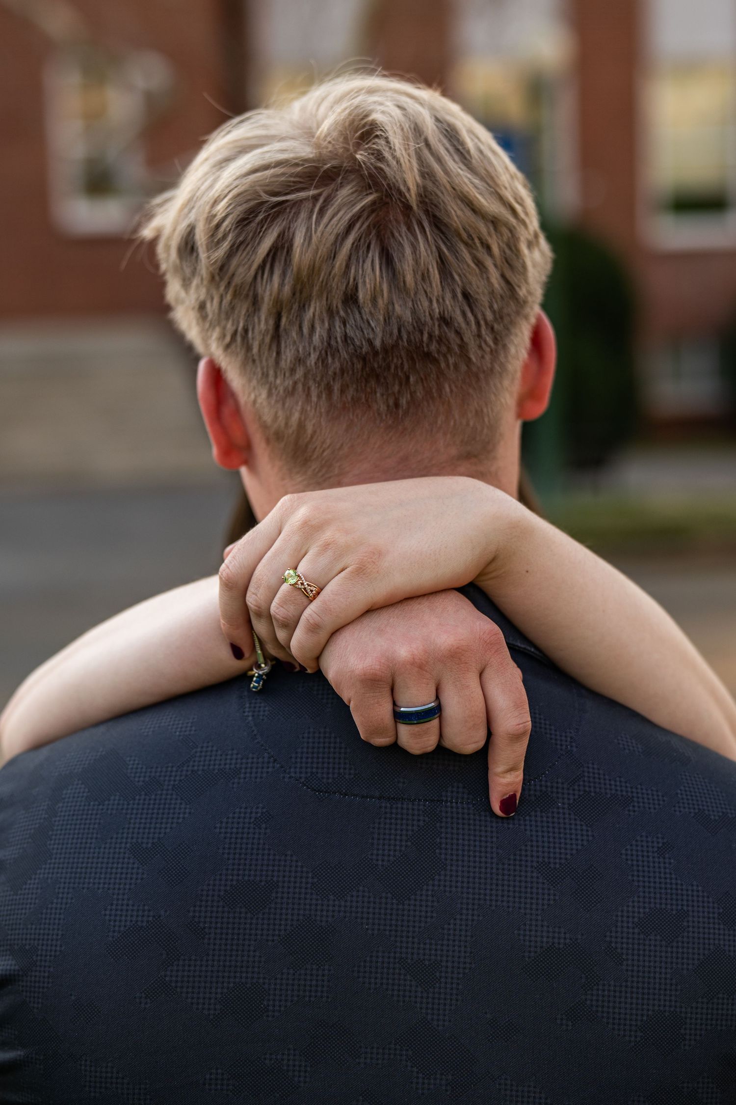 Close-up view of hands with wedding rings embracing against a navy blue shirt.
