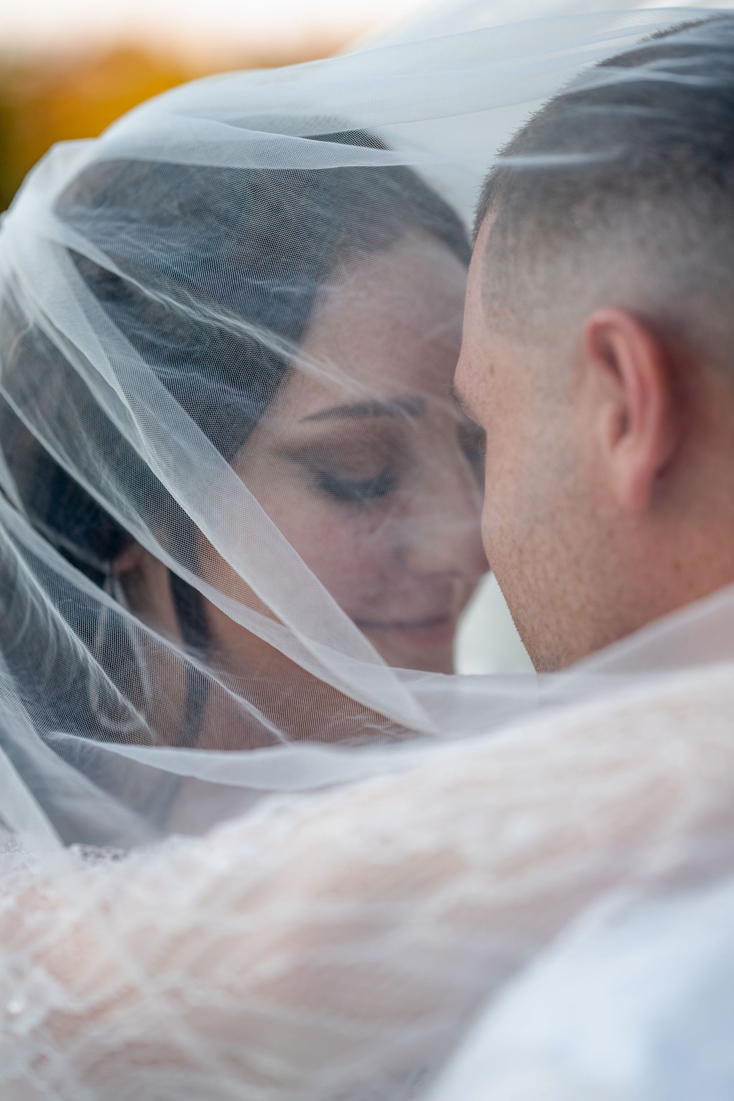 Close-up shot of a bride and groom under a delicate white veil.