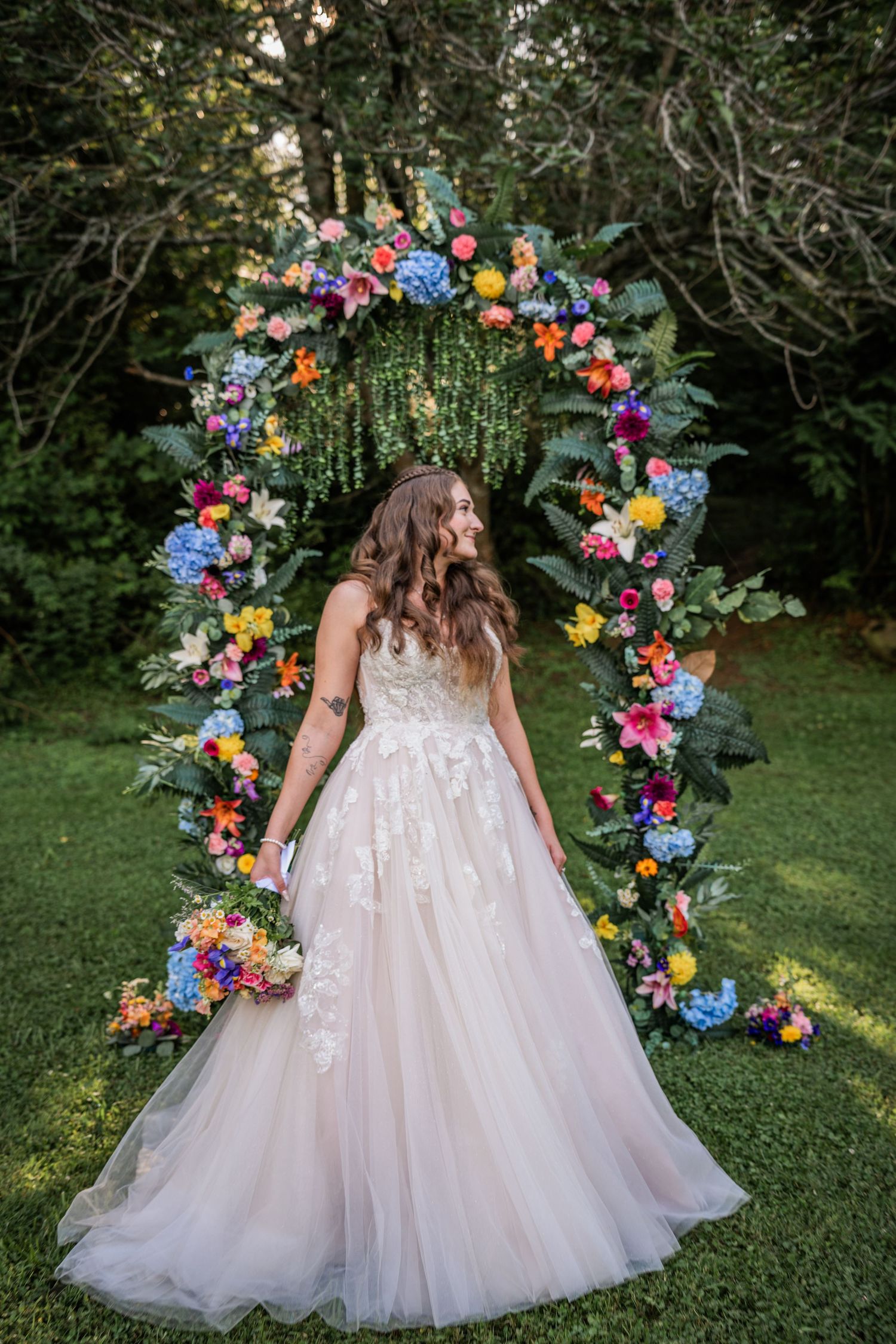 Wedding dress with tulle skirt against colorful floral arch in garden setting.