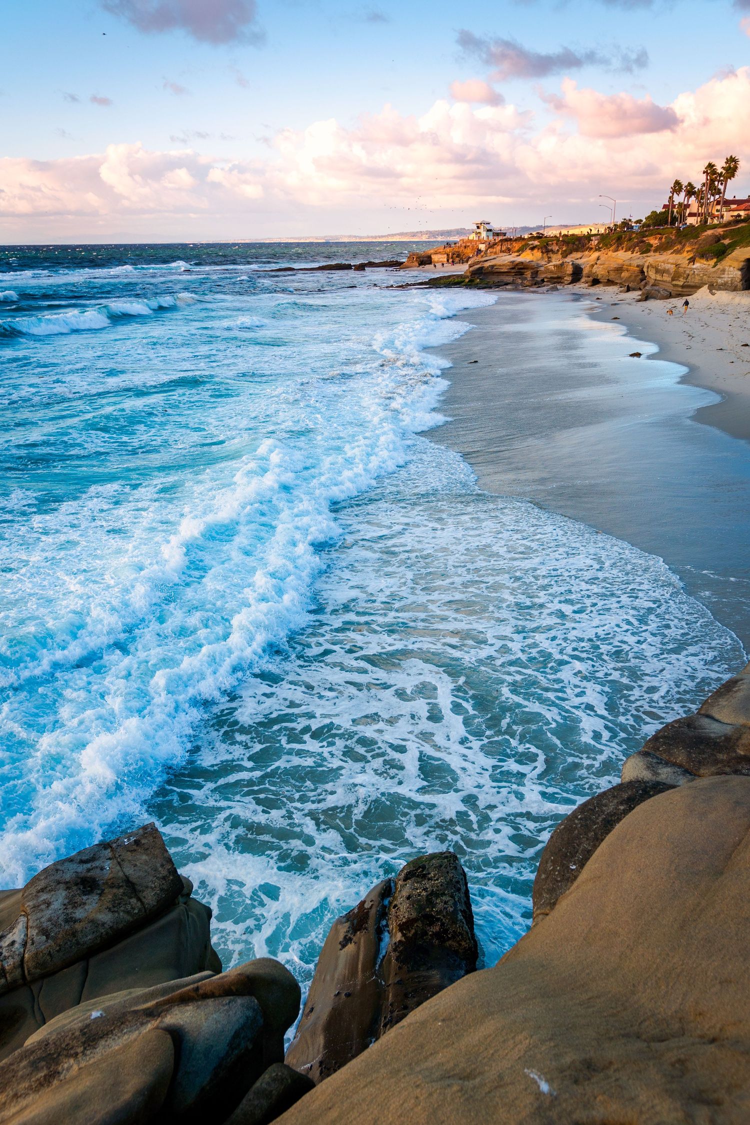 Dramatic ocean waves crashing against rocky coastline during golden hour.