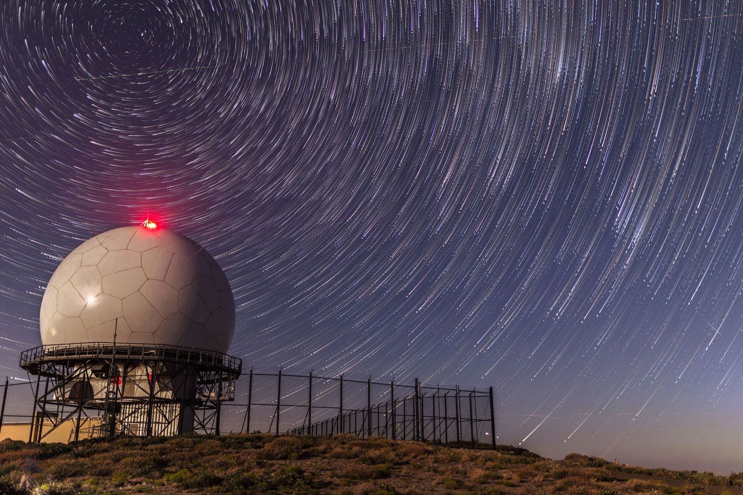 Long exposure night sky photography showing star trails and observatory domes.
