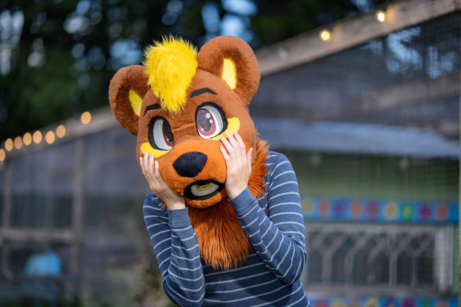 Person wearing a fursuit with orange ears and striped shirt poses in an outdoor setting at dusk.