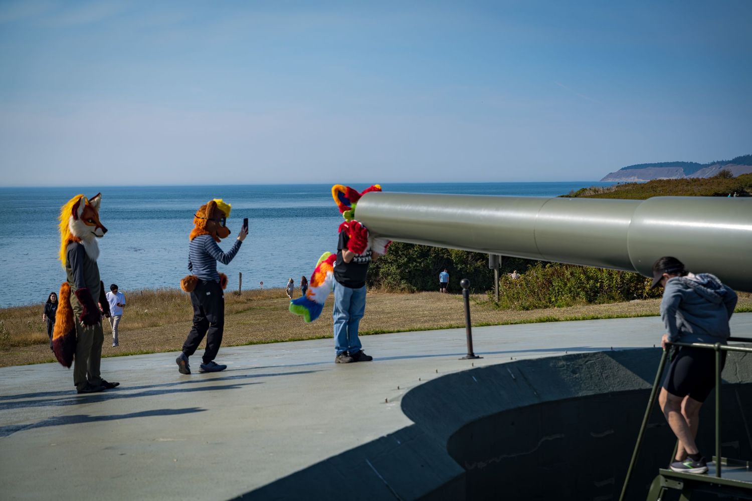 People explore a coastal defense bunker overlooking the ocean on a sunny day.