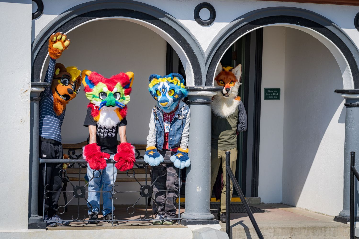 Colorful fursuit characters pose under decorative arches of a historic building.