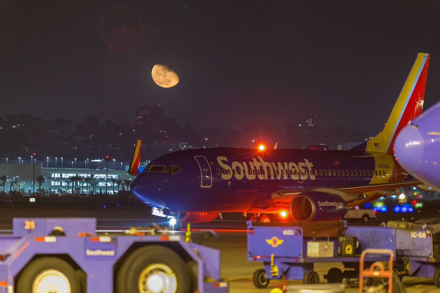 Commercial aircraft parked at gates during nighttime with illuminated terminal lights.