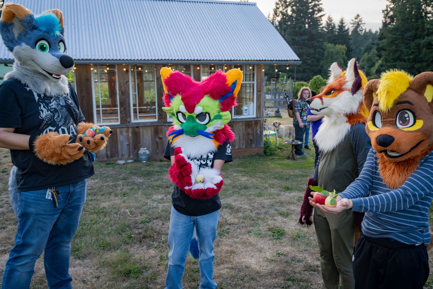 Costumed performers gather outside a rural building with pine trees in the background.