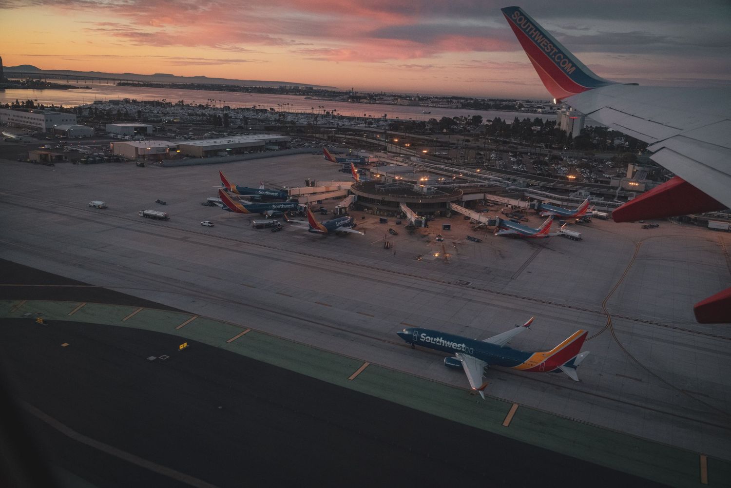 Aerial view of commercial airplanes on airport tarmac during sunset with red-tinted wing visible in frame.