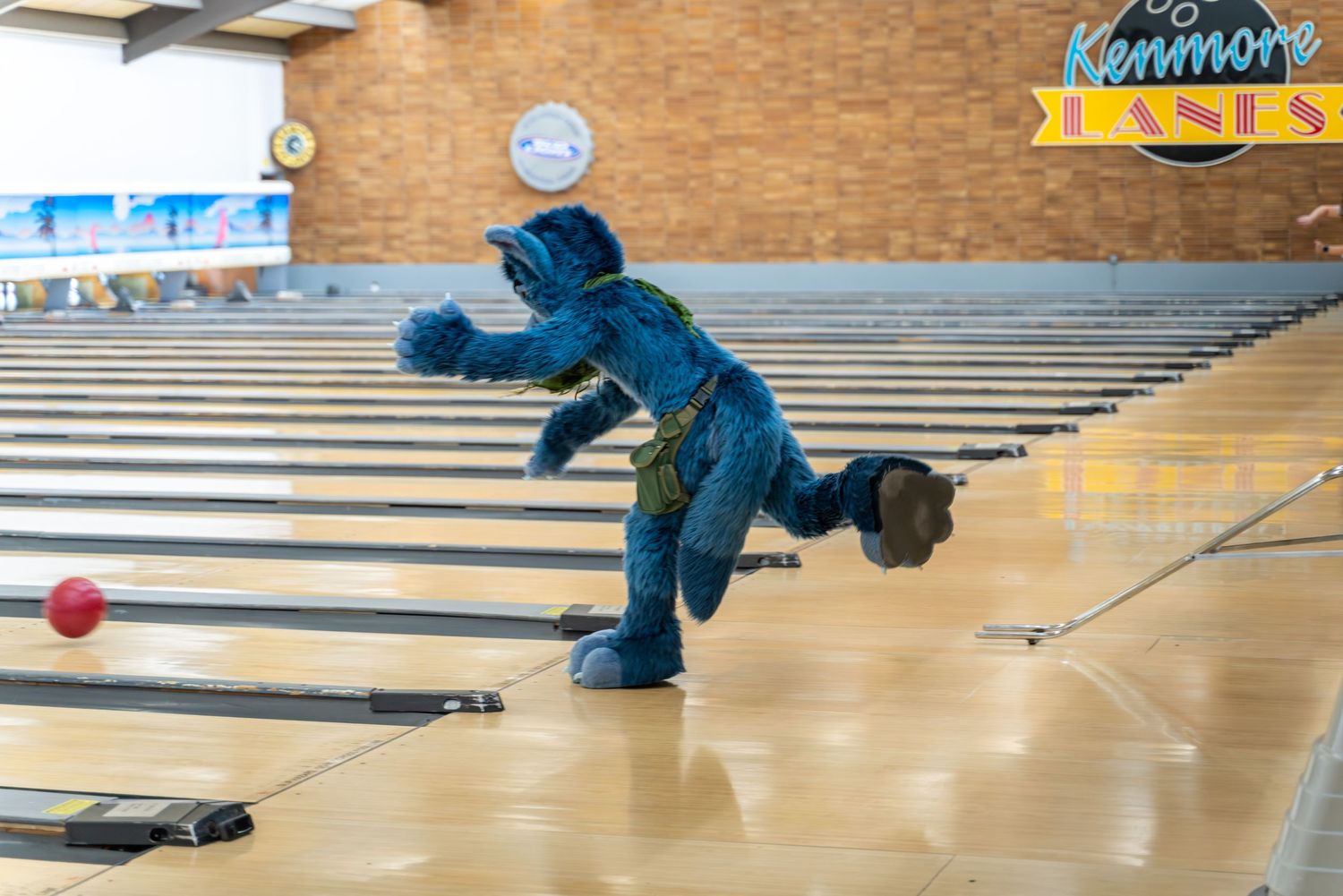 Bowler in blue fursuit crouched in follow-through position after releasing ball.