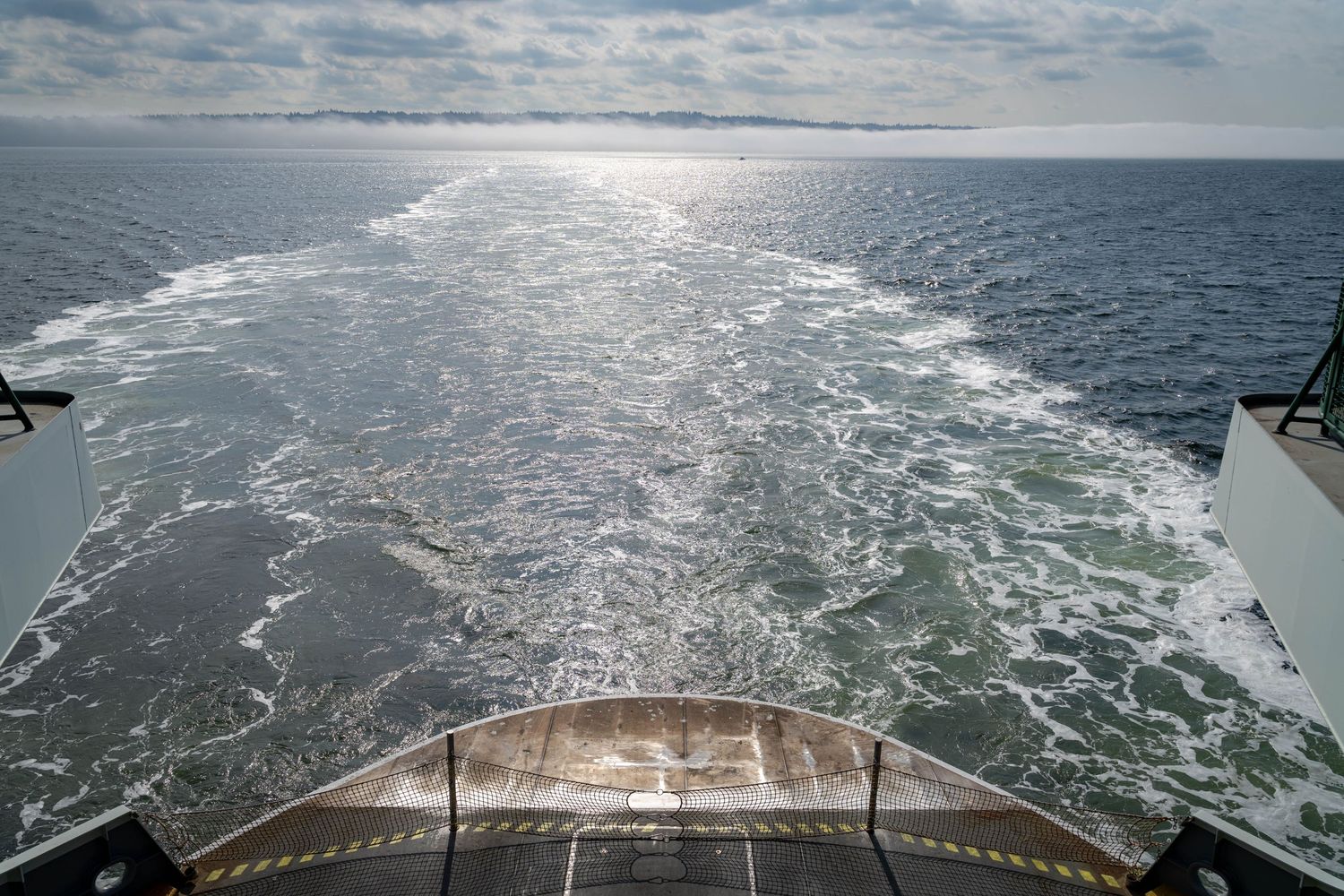 Wake view from the stern of a ferry boat showing the churning water trail across a calm sea.
