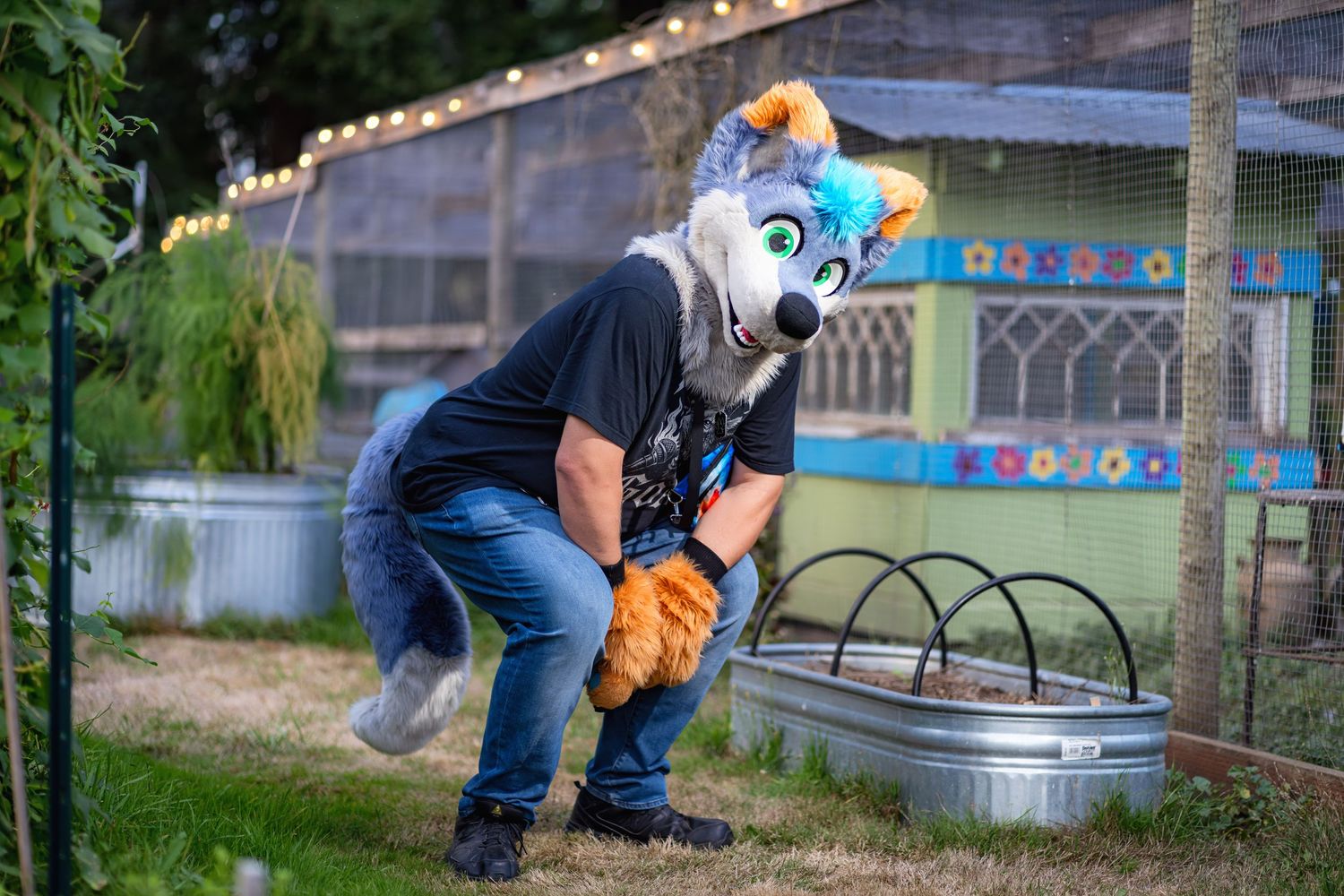 Fursuit characters in casual attire pose near garden fixtures with string lights overhead.