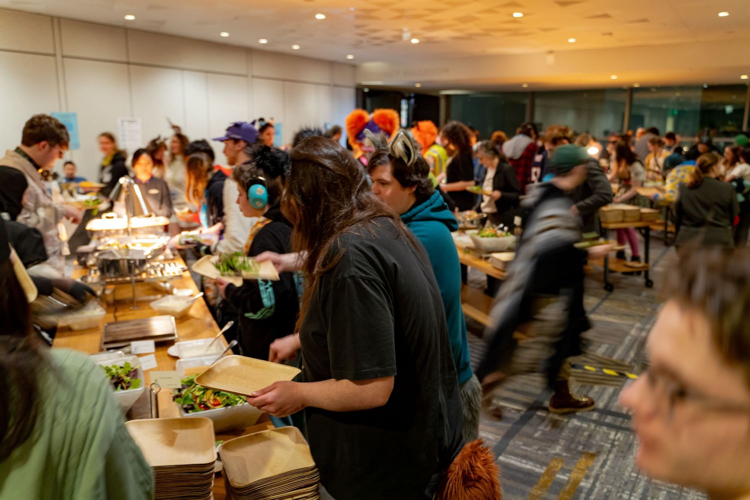 A large group of people gathered around tables in a crowded dining hall or restaurant space.