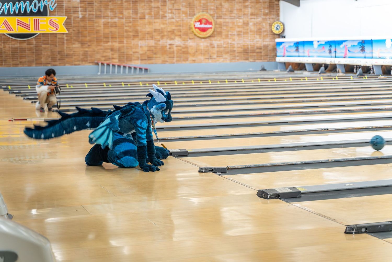 Person in fursuit showing bowling form while releasing ball down polished lane.