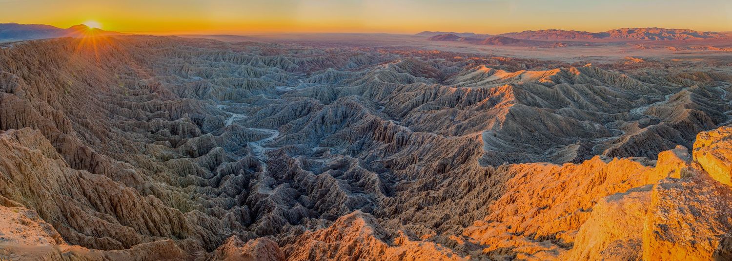 Panoramic sunset view of rugged mountains with dramatic orange sky and shadows in the canyons.