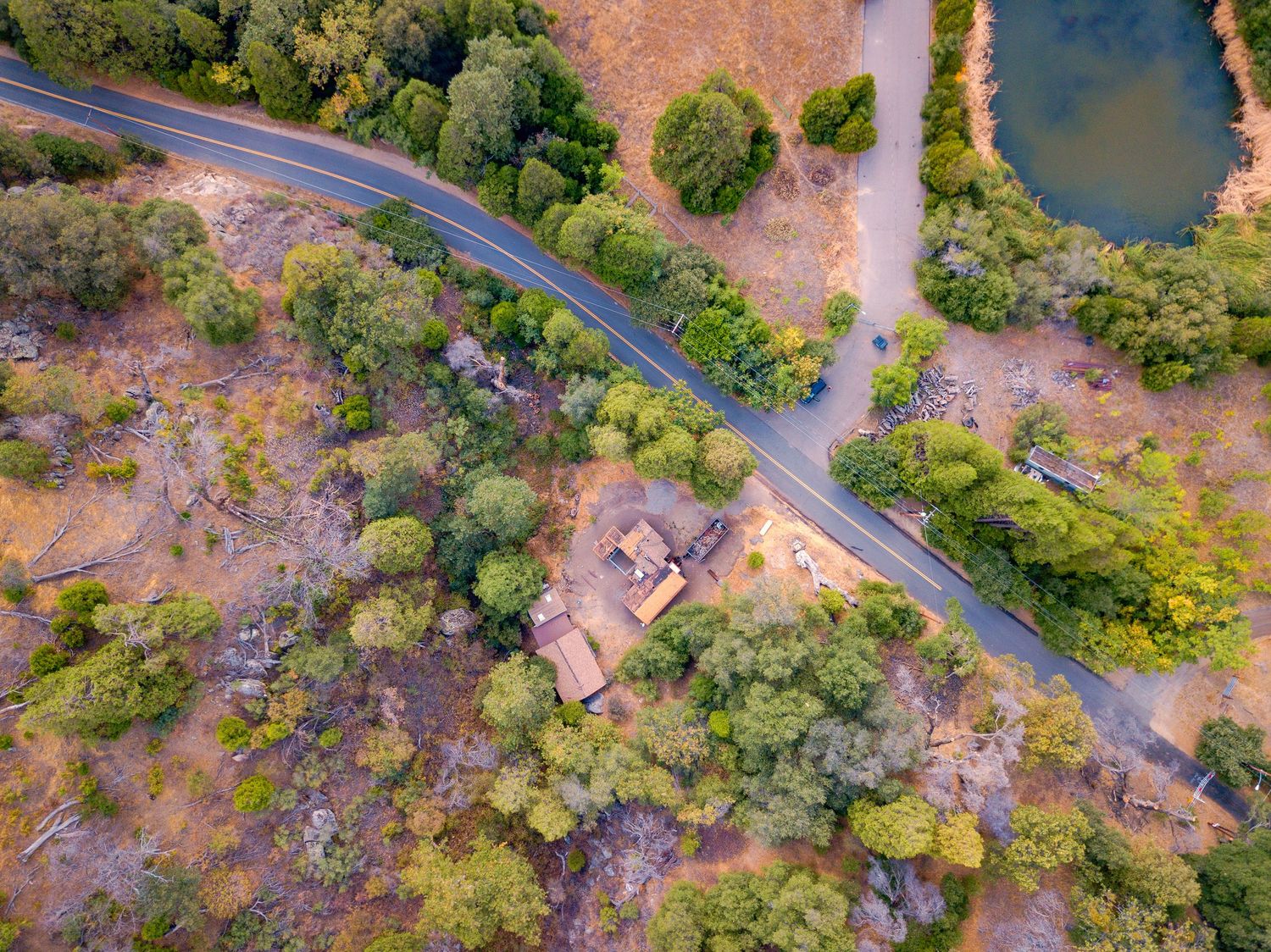 Winding road through lush forest landscape captured from above with river views.