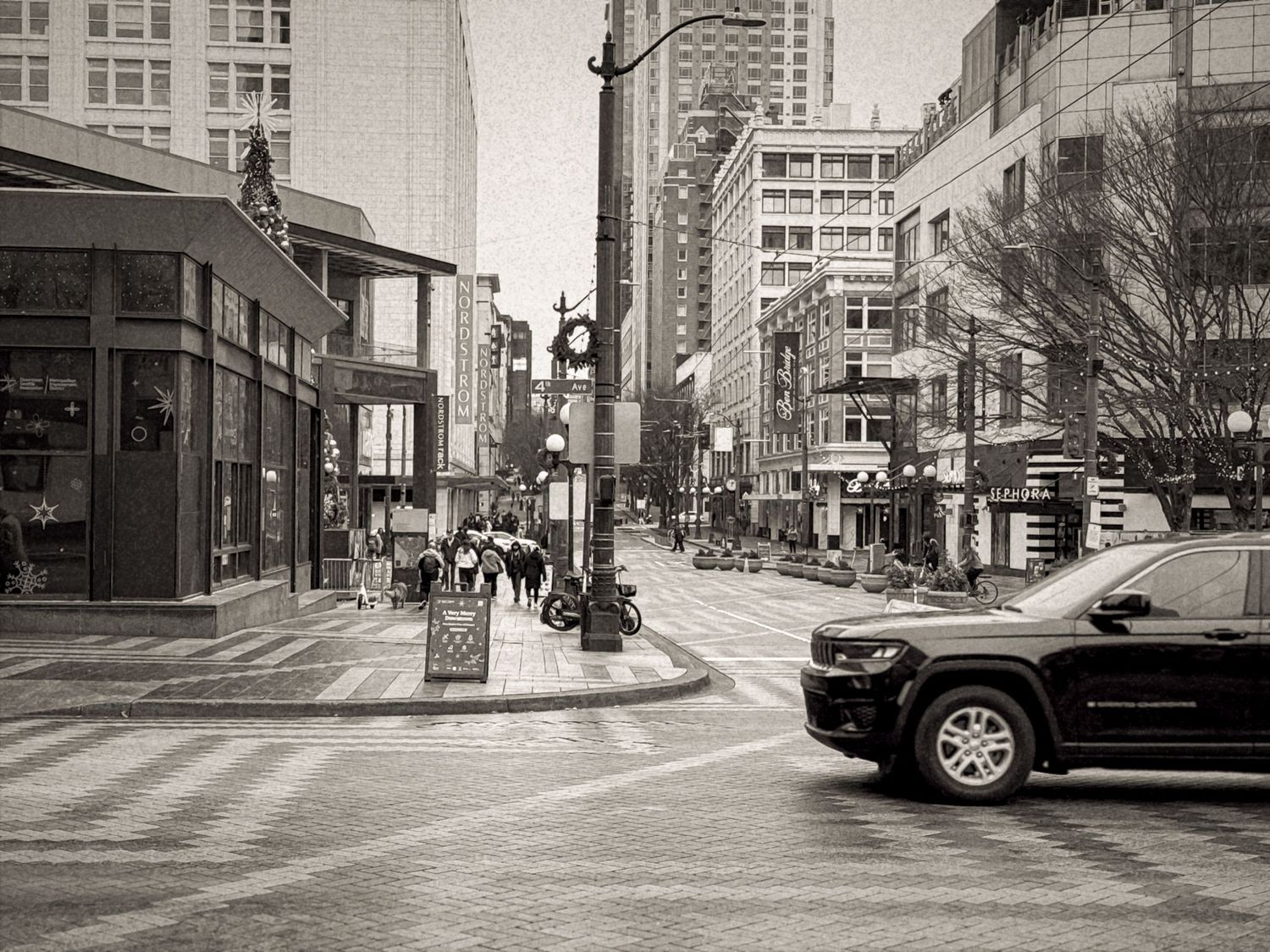 Black and white urban street scene with tall buildings and cars in a city downtown area.