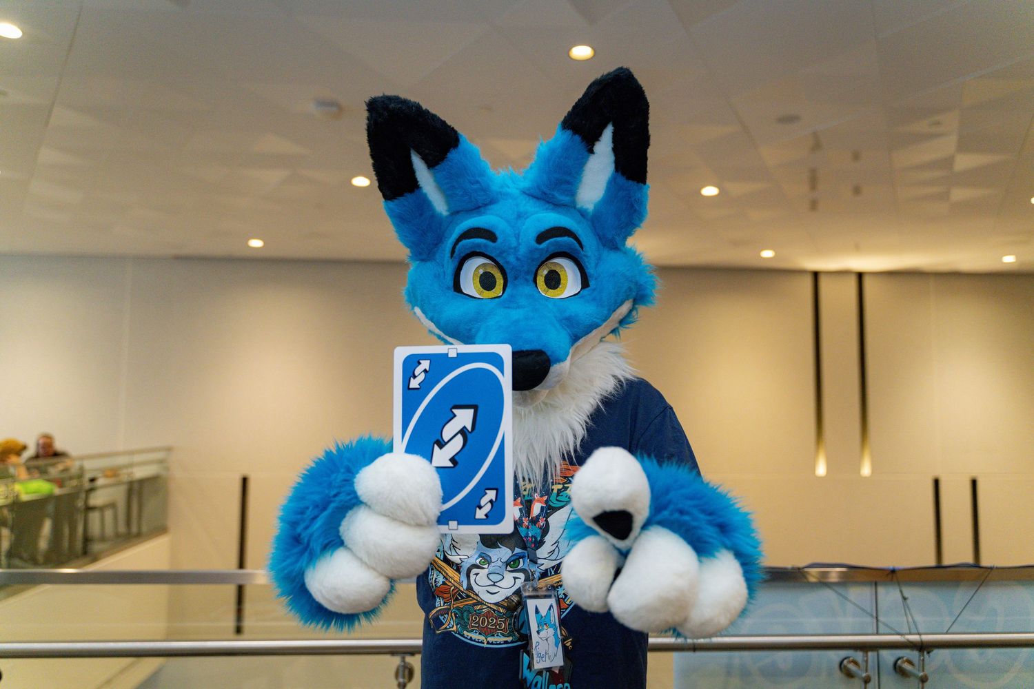 A large blue and white mascot character stands in an office space with recessed lighting.