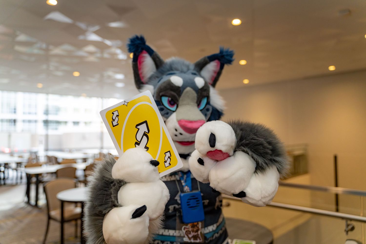 Large plush mascot character sits at a cafeteria table in an empty dining hall.