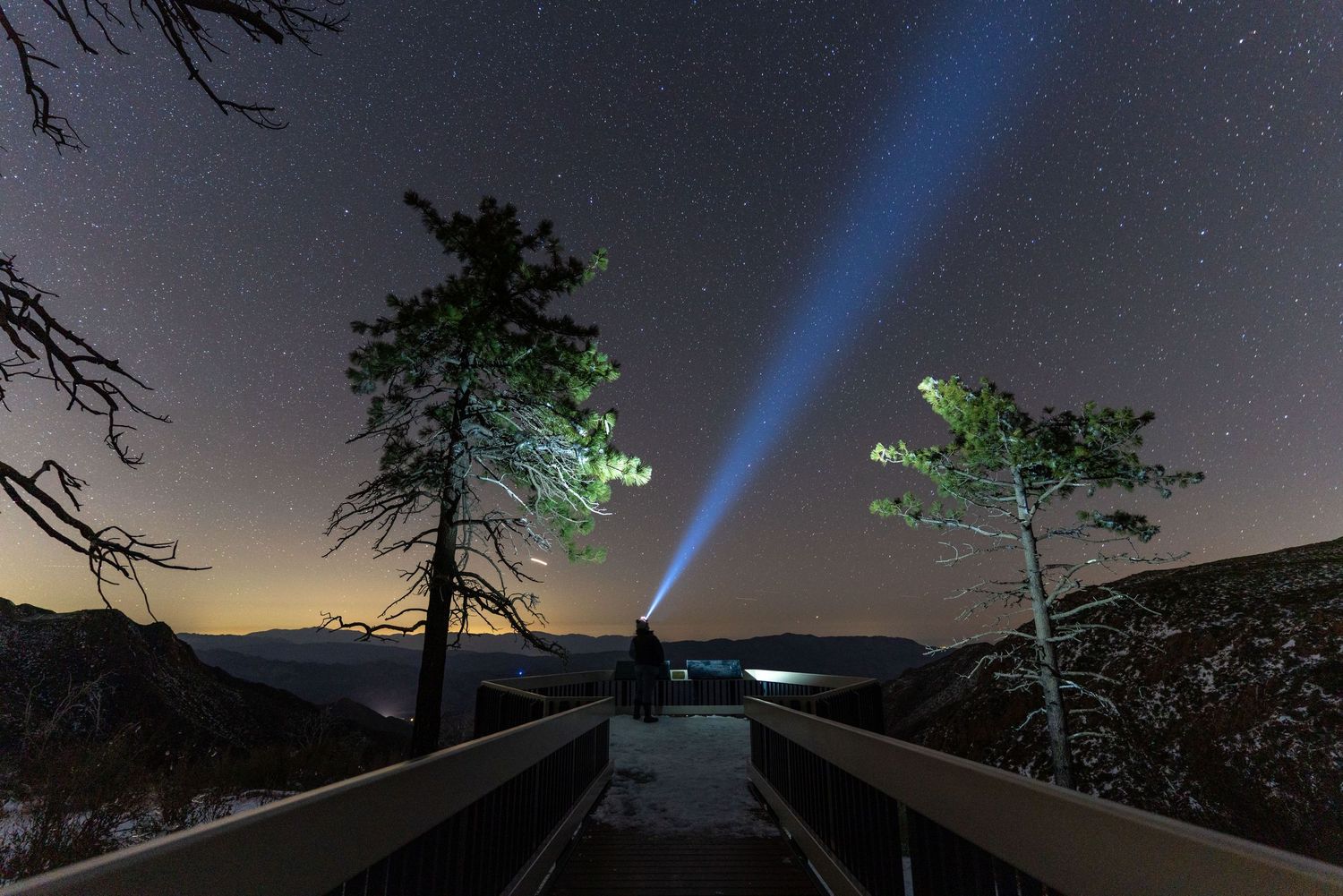 Night sky panorama with bright beam of light reaching upward through starry darkness.