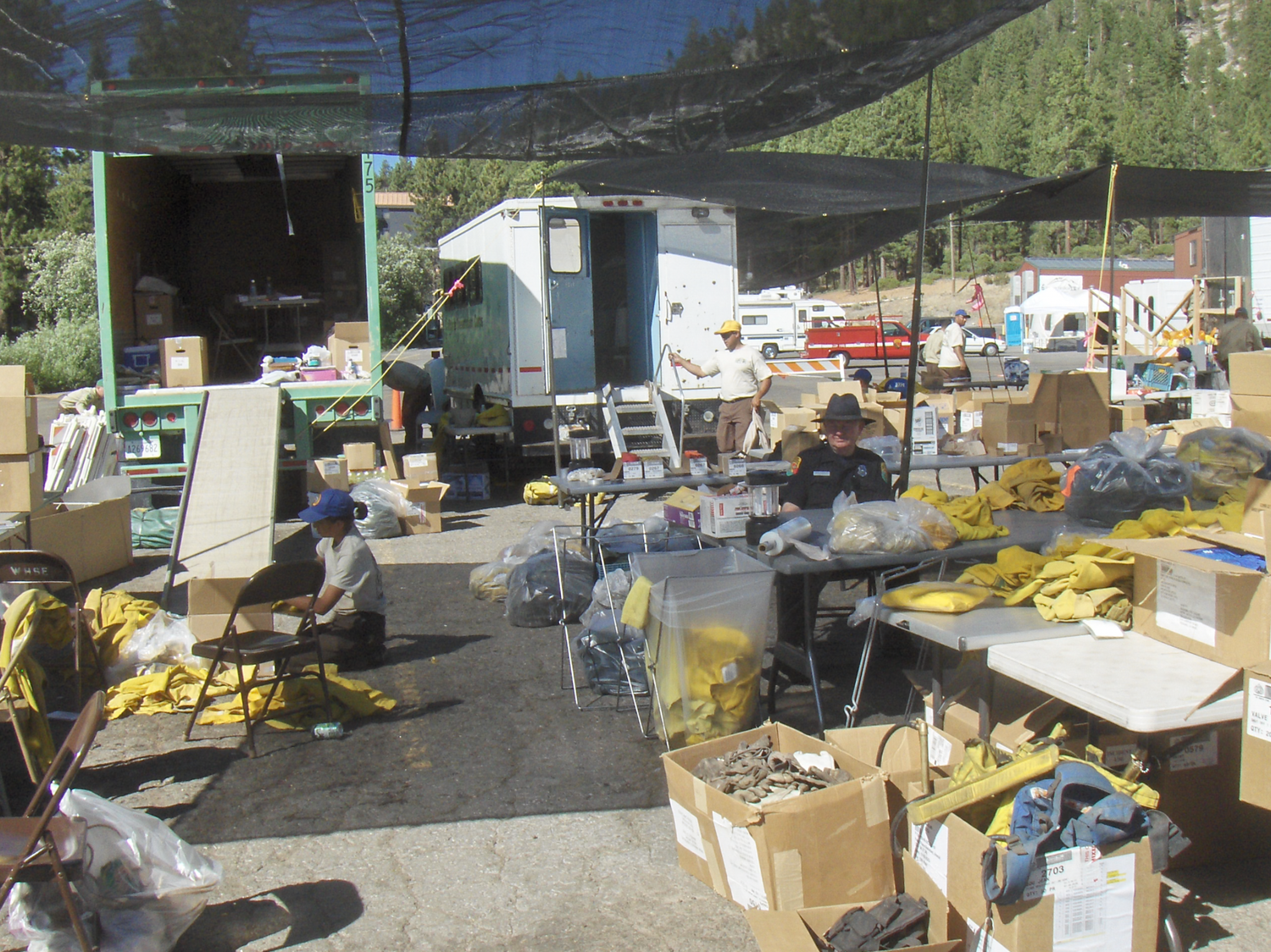Outdoor staging area with supplies, equipment and vehicles arranged under blue tarps.