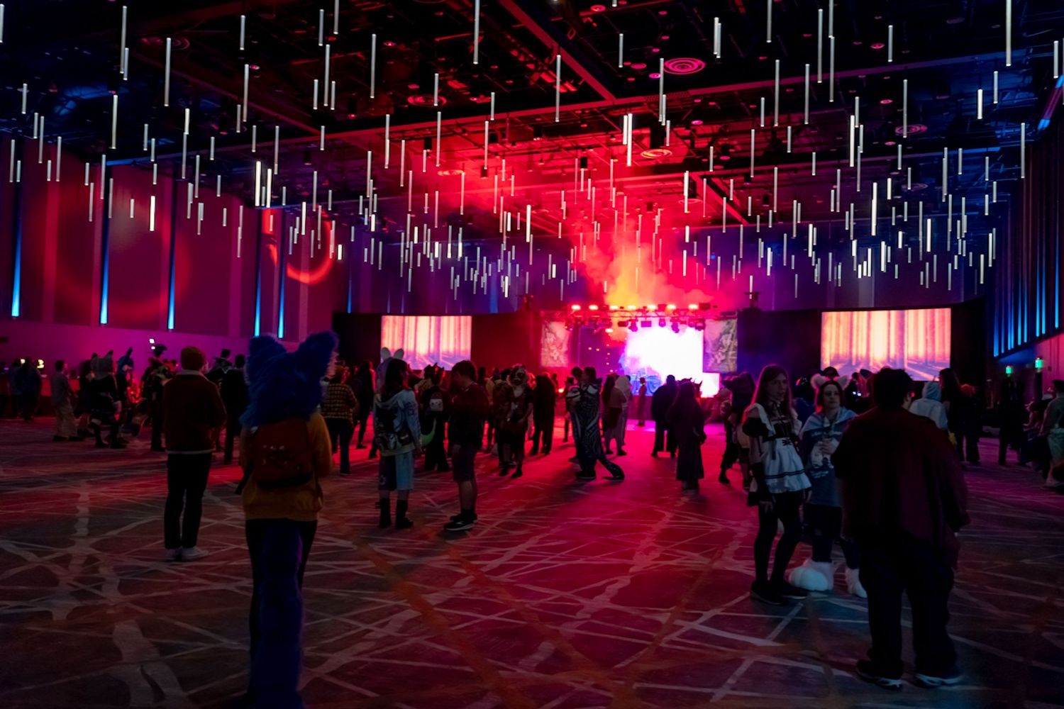 A crowd gathers at night with red flares and emergency lights illuminating the dark urban scene.
