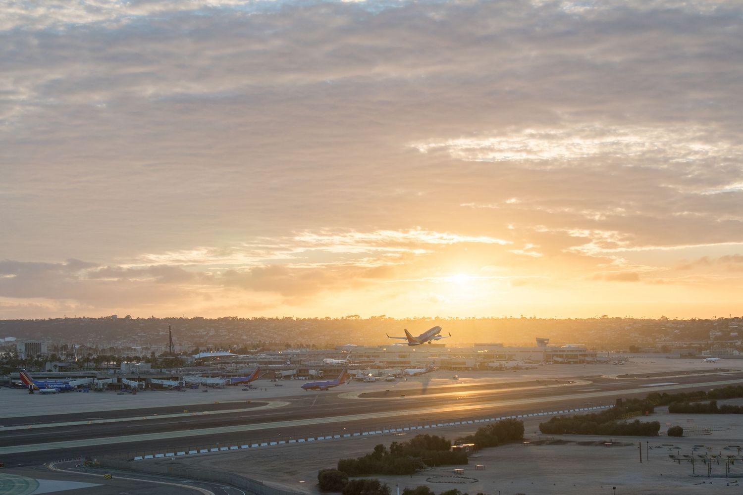 Airport runway panorama at sunset with golden clouds and orange sky over the tarmac.