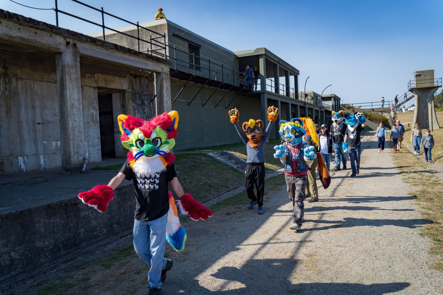 Costumed figures walk along a sunny concrete path with ocean views.