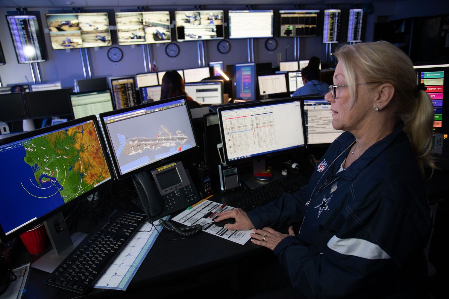 Dark control room with multiple computer monitors displaying weather and tracking data.