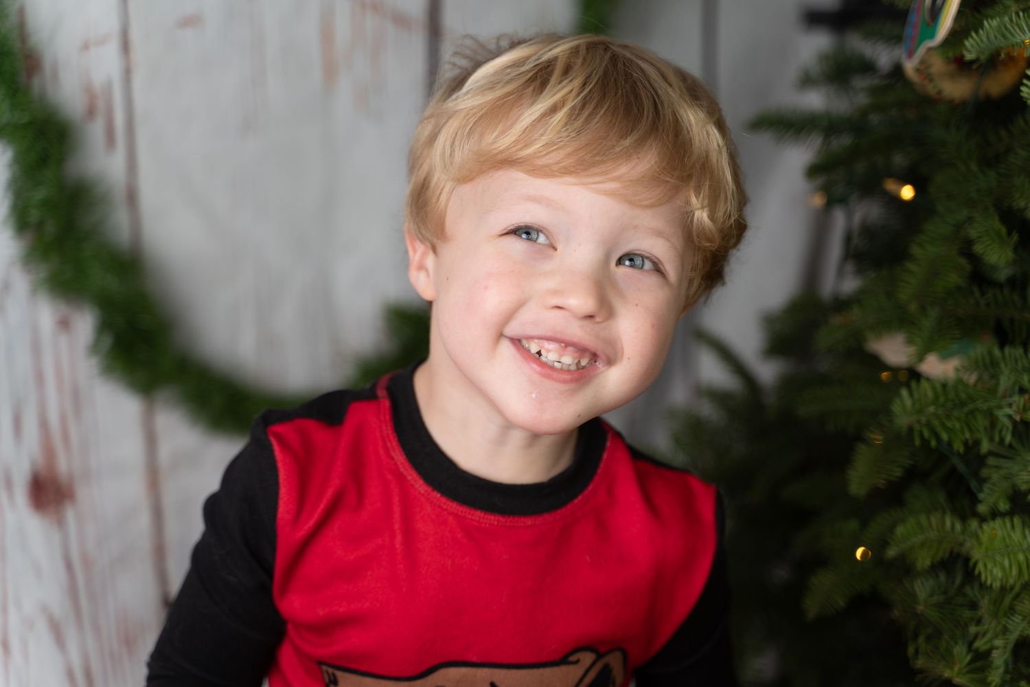 Young child smiling in red outfit with holiday decorations in background.