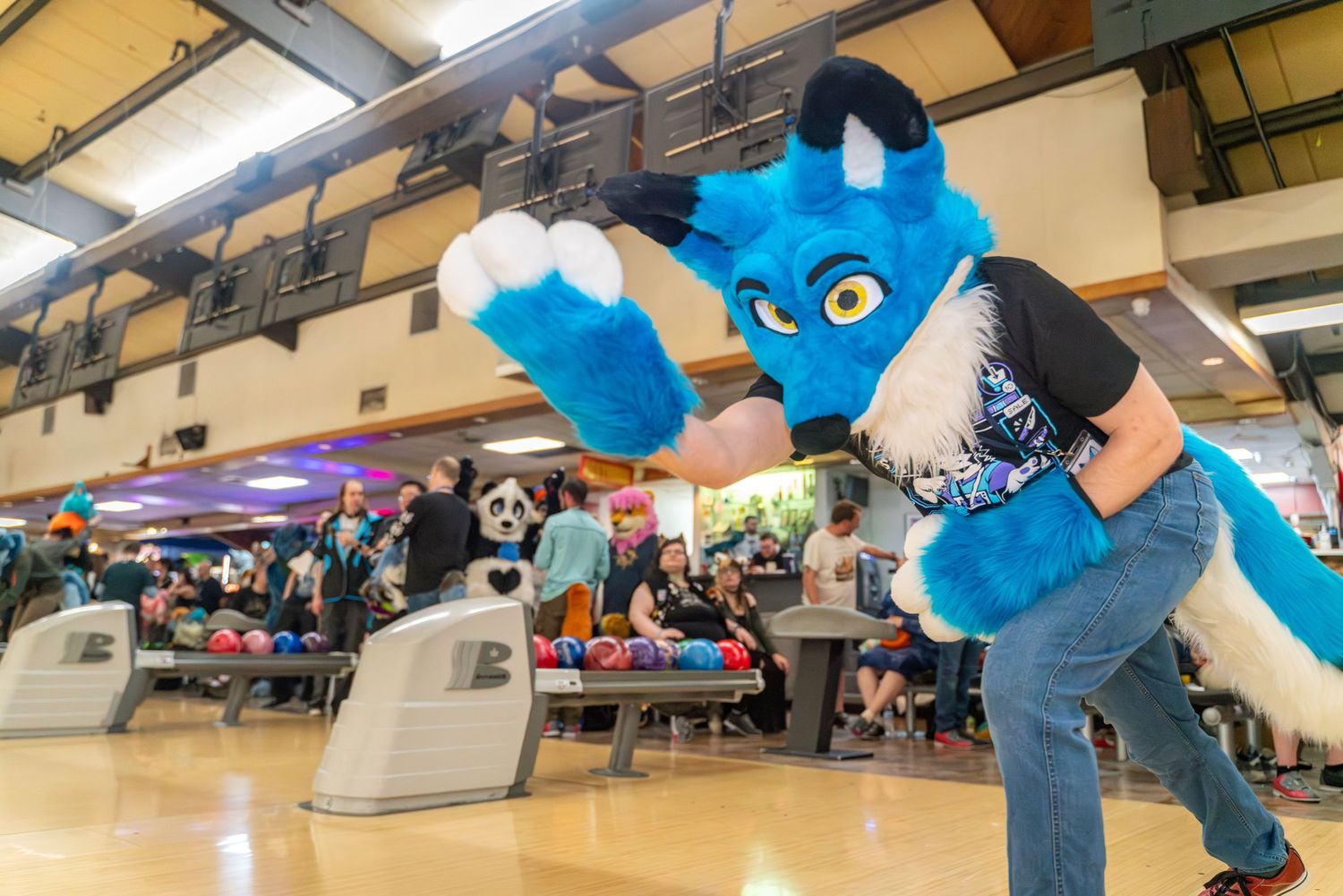 Multiple blue fursuit characters arranged in a line at a bowling alley.