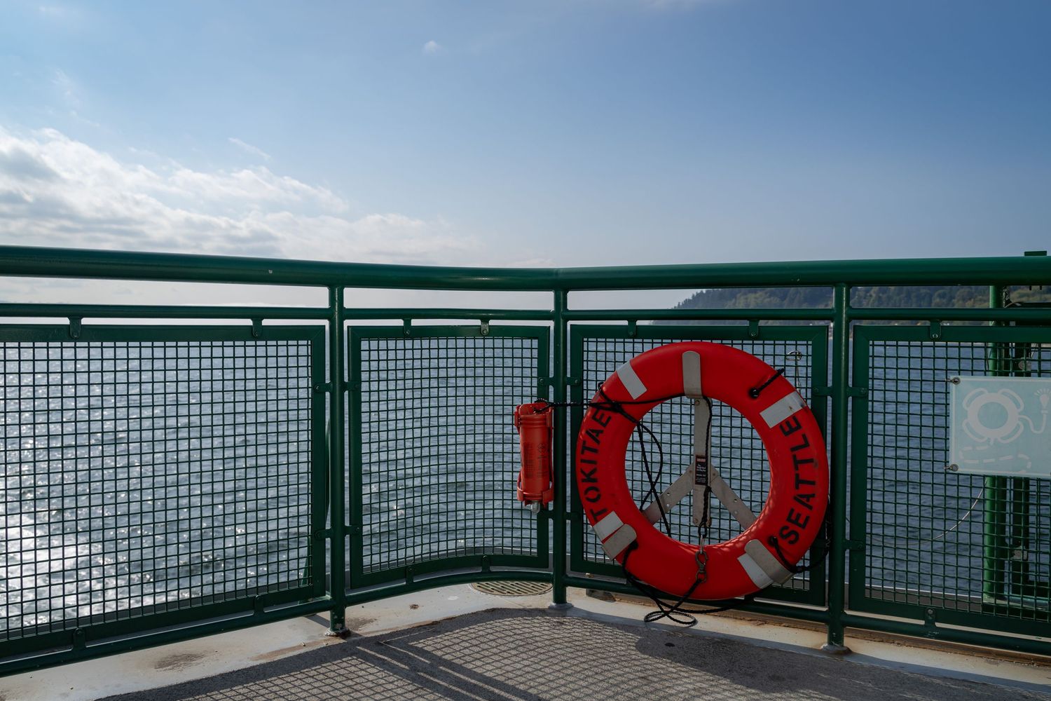 Ferry deck railing with orange life preservers mounted along green metal barriers.