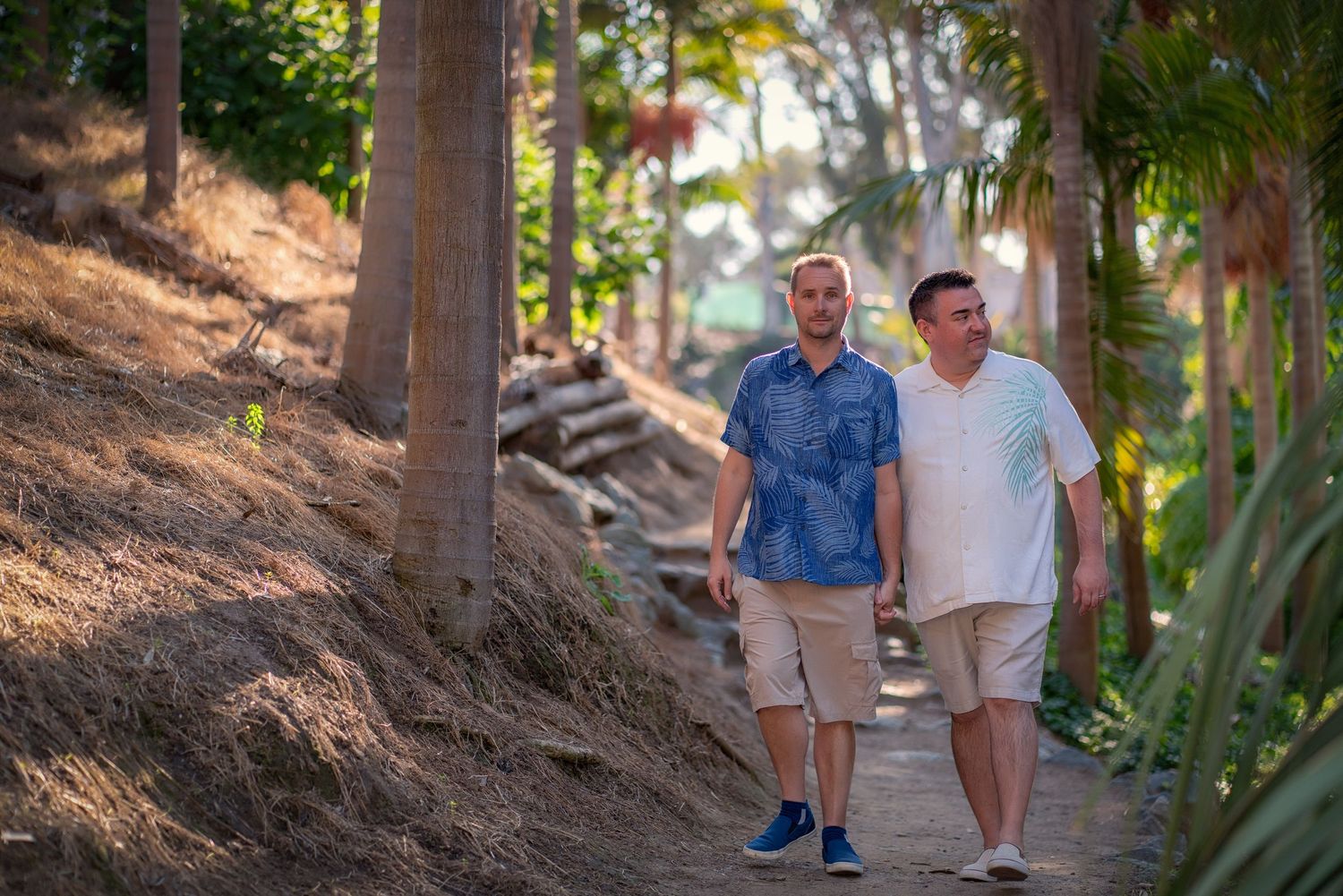 Two people walking together on a palm-lined path in casual summer attire.