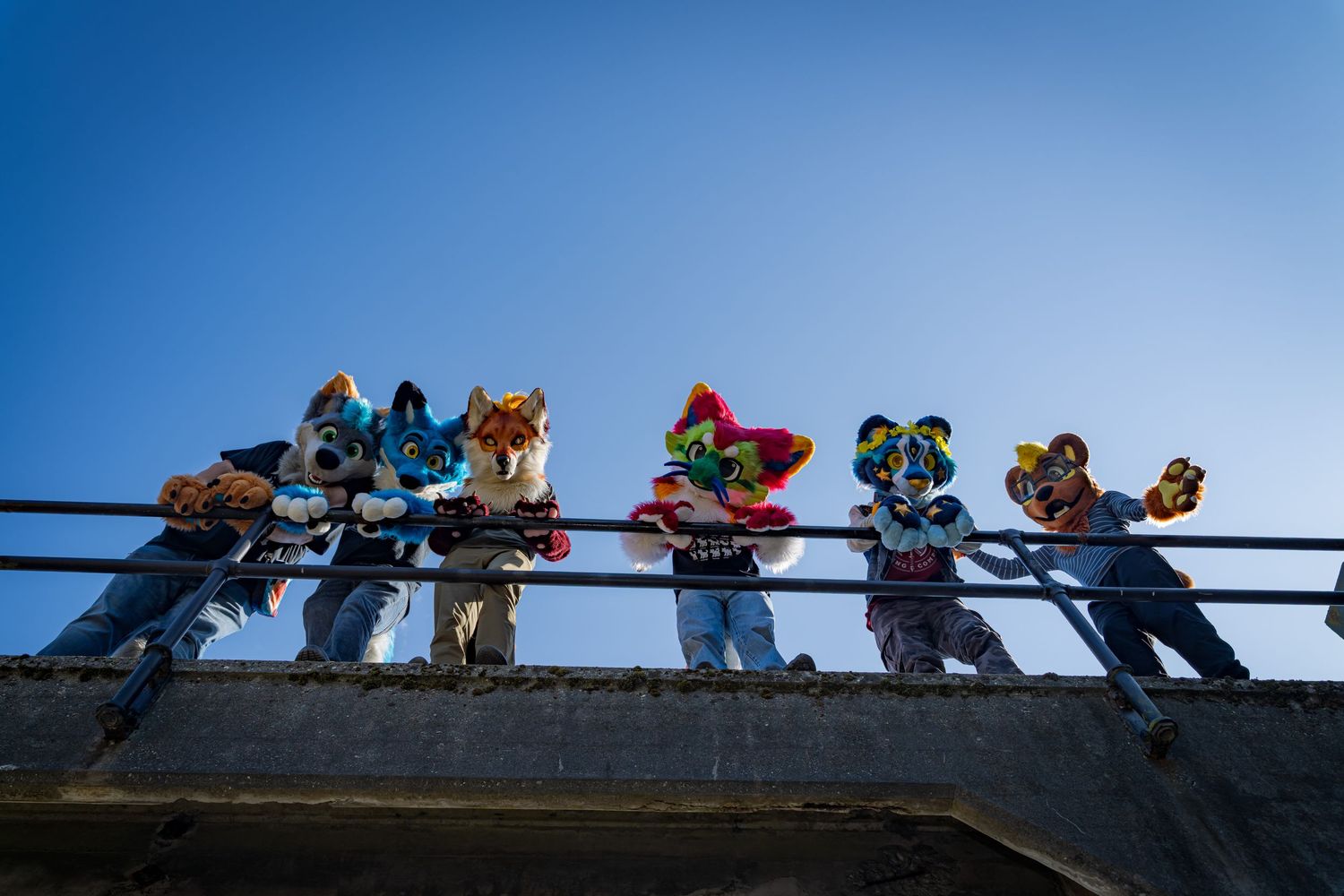 Row of fursuiters lined up along metal railings photographed from below.