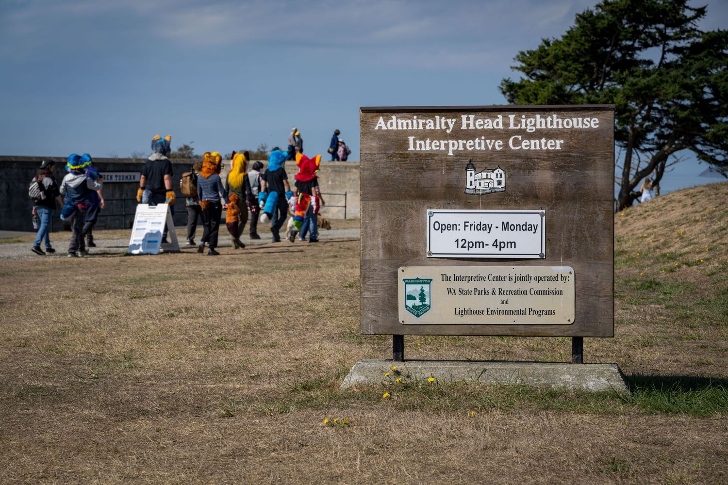Sign for Admiralty Head Lighthouse Interpretive Centre with visitors walking nearby.