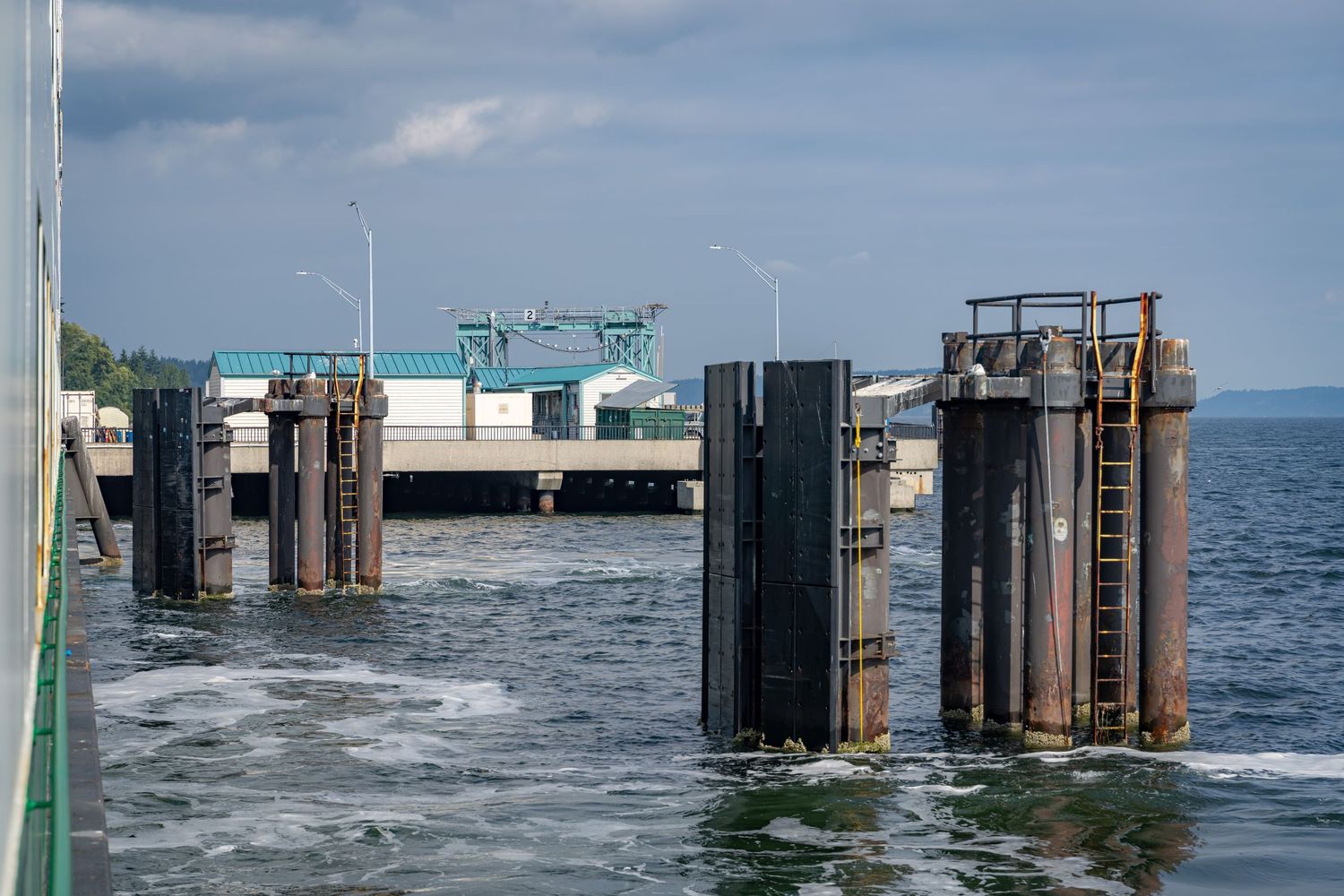 Ferry dock pilings and loading ramp structure extending into blue water on a sunny day.