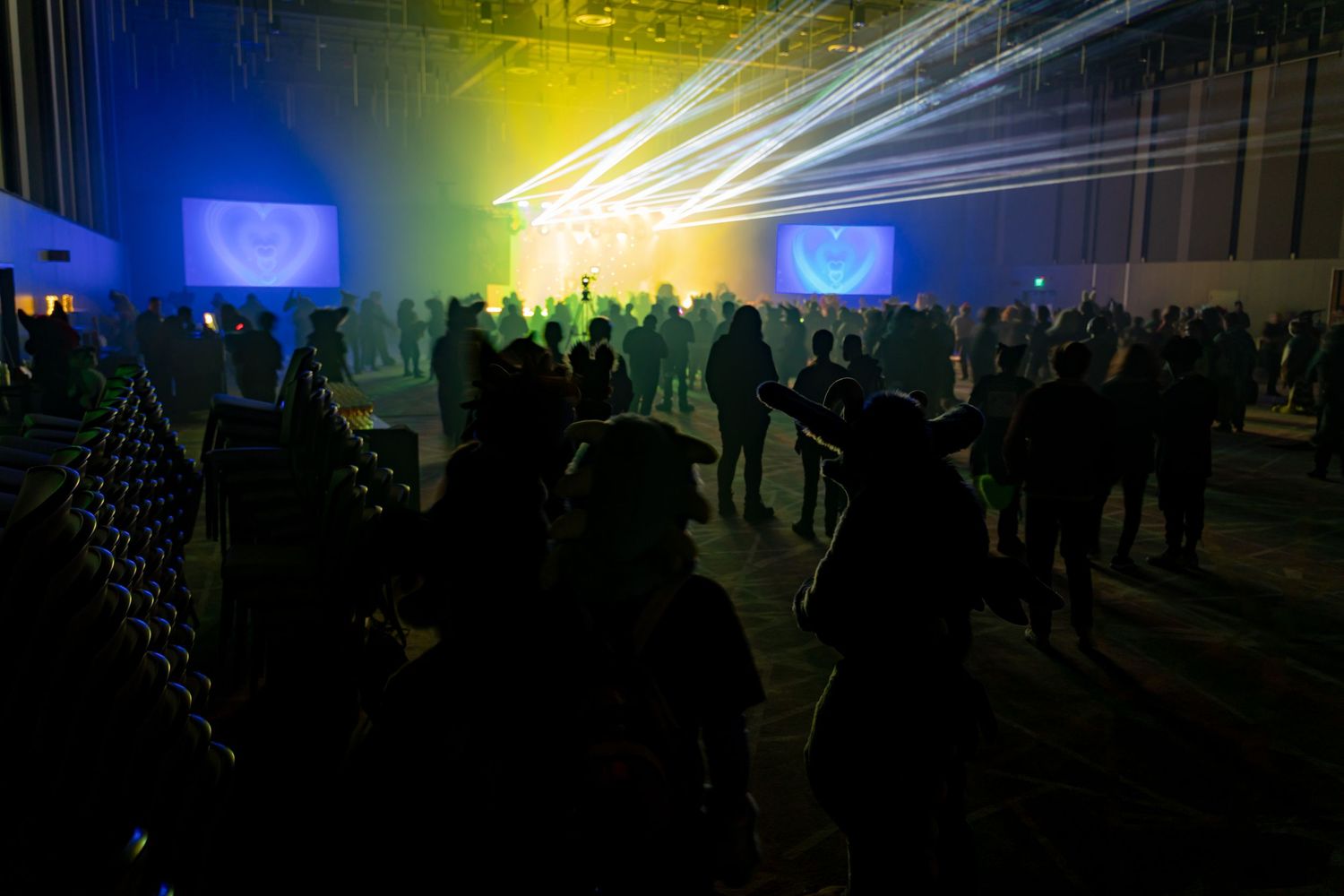 Silhouettes of concert crowd against bright yellow and blue stage lighting effects at a nighttime performance.