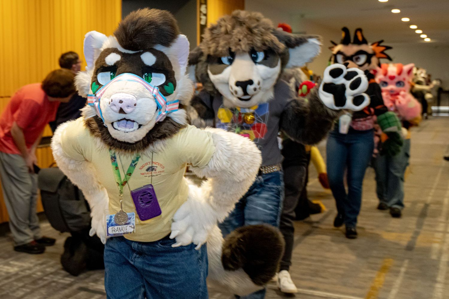 A group of fursuit characters pose and interact at an indoor convention space with bright lighting.