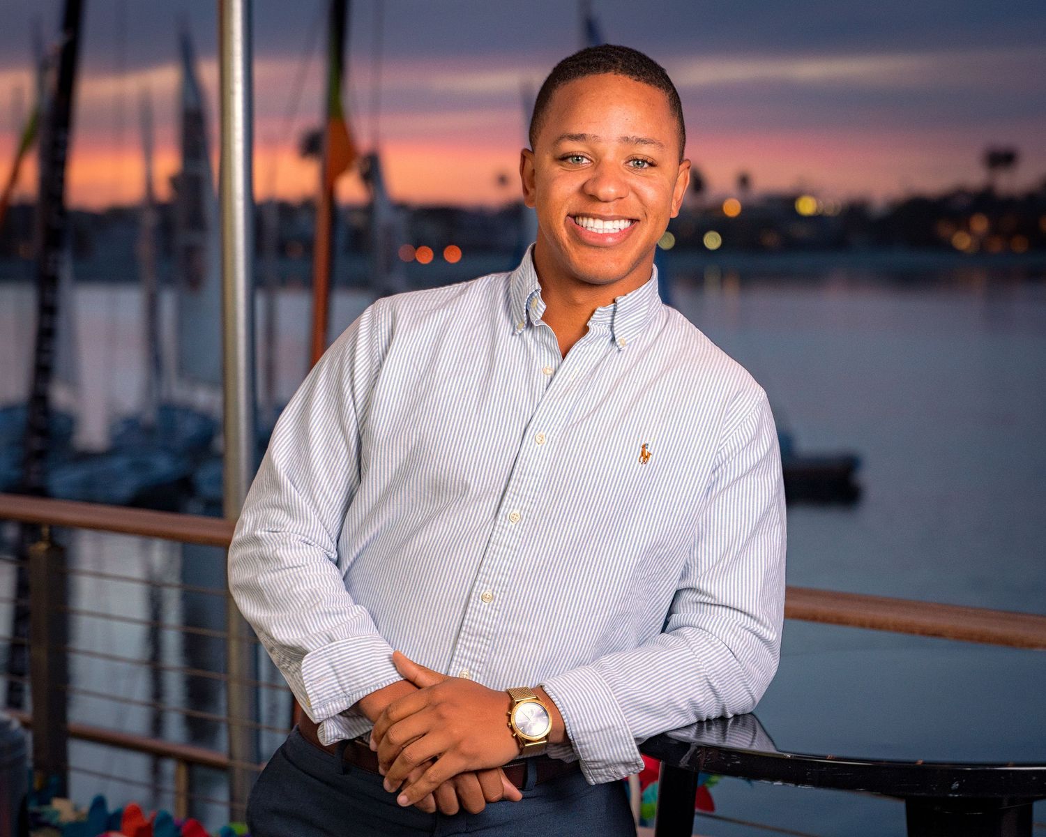 Professional portrait captured at sunset by the waterfront with boats in background.