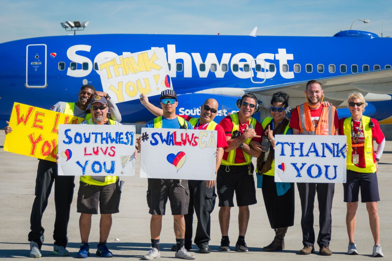 Southwest Airlines employees holding colorful thank you signs on airport tarmac.