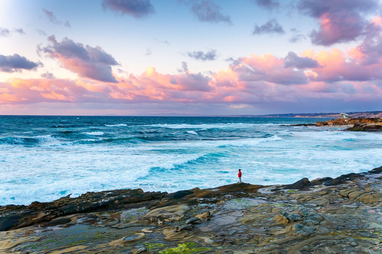 Panoramic seascape with dramatic sunset clouds over rocky coastal shoreline.