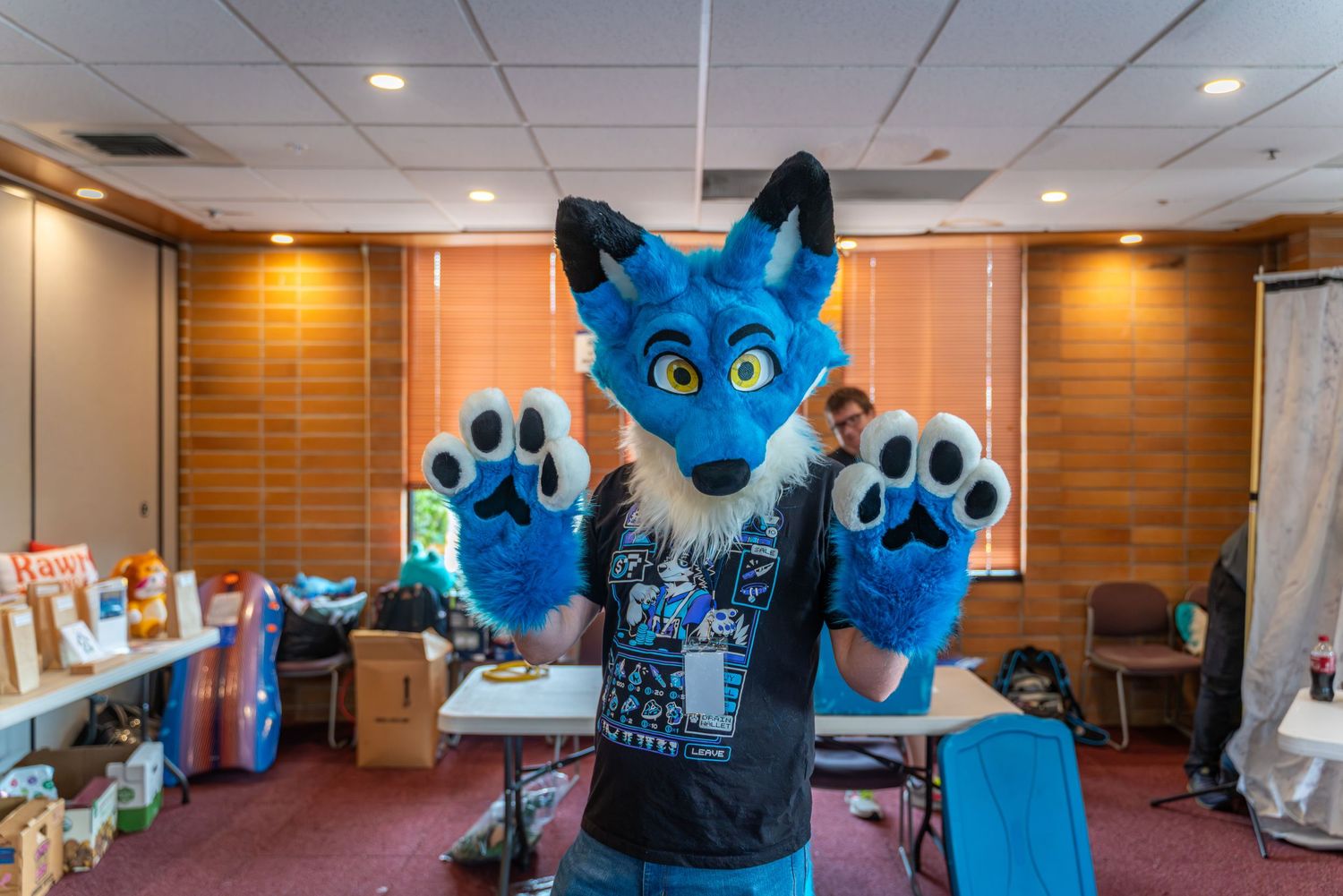 Blue furry mascot characters pose together at an indoor event venue with wood paneled walls.