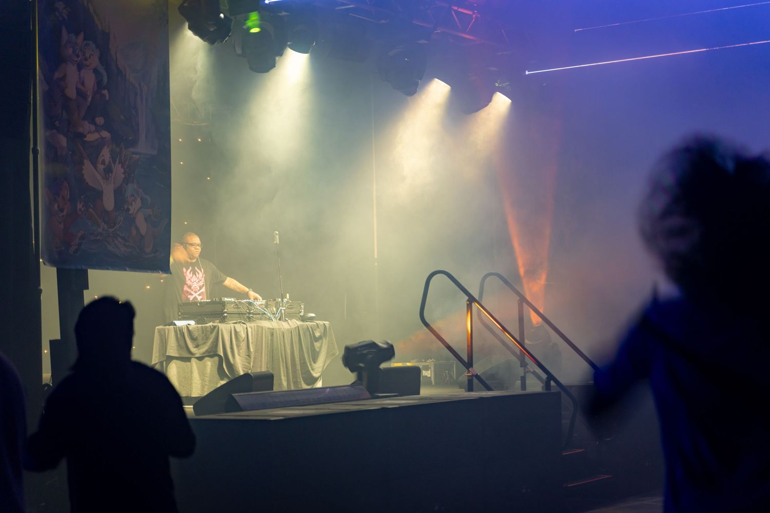 Concert stage lit with colorful lights and fog effects showing silhouettes of performers and equipment.