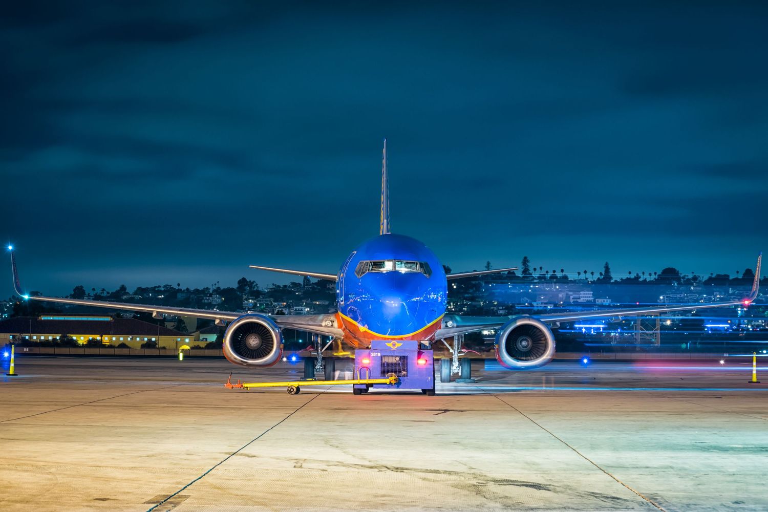 Commercial airplanes parked at night with blue lighting and illuminated terminal in background.